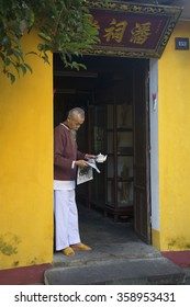 HOI AN, VIETNAM - JANUARY 04, 2016: An Old Man Brews Tea And Reads The Newspaper On The Doorstep Of The Old House