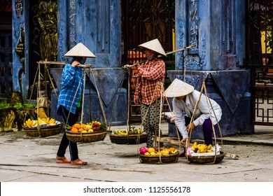Hoi An/Vietnam - 01-03-2017: Vietnamese wearing typical conical hat selling fruit in a bamboo carrying pole with double basket at Hoi An Street
