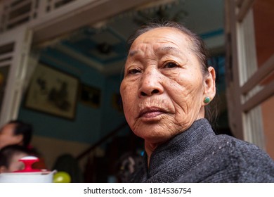 Hoi An / Vietnam - January 18, 2020: Portrait Of Pretty Vietnamese Older Woman In Traditional Dress Sitting At Her Front Door