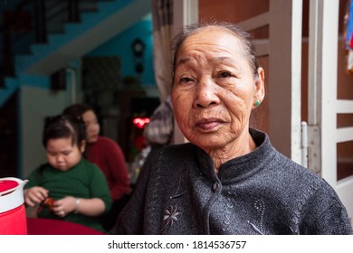 Hoi An / Vietnam - January 18, 2020: Portrait Of Pretty Vietnamese Older Woman In Traditional Dress Sitting At Her Front Door