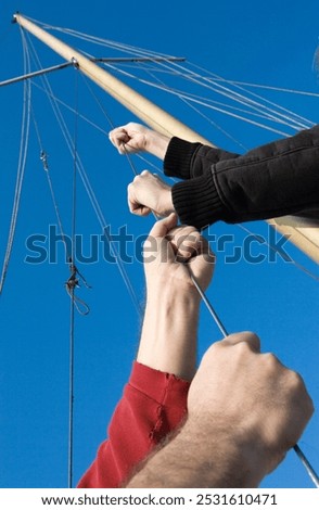 Hoisting the sails. Hands pulling on a rop at a sailingboat. Mast en ropes.