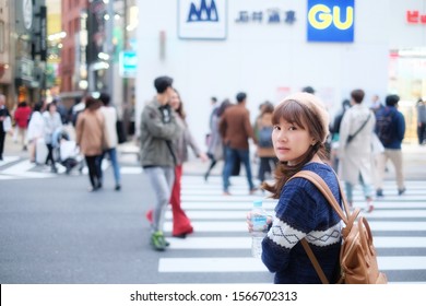 Hokkaido, Japan - November 16, 2018: Beautiful Asia woman in blue sweater, cream hat and shoulder brown bag  walking outside, turns around looks at the camera at crosswalk, Shibuya district, Tokyo   