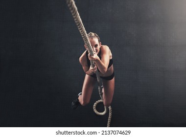 Hold On Tight Through Your Challenges. Shot Of A Sporty Young Woman Climbing A Rope In A Gym.