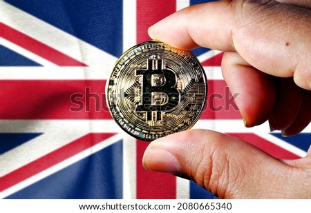 Hold the physical version of Bitcoin (the new virtual currency) and the British flag. UK cryptocurrency and blockchain technology investor concept map (the background is deliberately blurred) 