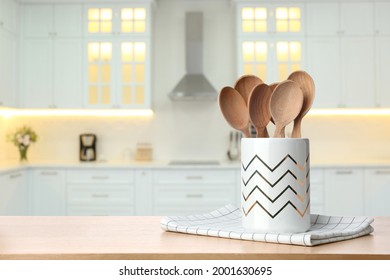 Holder with spoons on wooden table and blurred view of stylish kitchen interior. Mockup for design