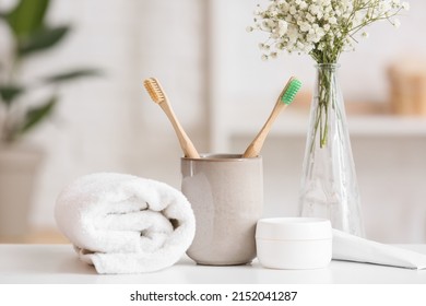 Holder with toothbrushes, jar of cream and rolled towel on table