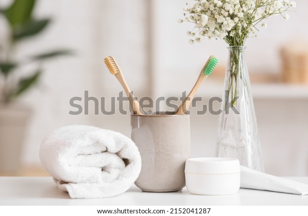 Holder with toothbrushes, jar of cream and rolled\
towel on table