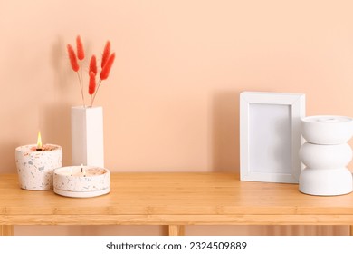 Holders with burning candles and blank frame on table near beige wall in room