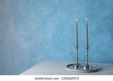 Holders with burning candles on wooden table near light blue wall, space for text