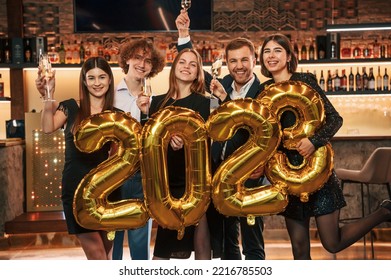 Holding 2023 New Year Ballons. Group of people in beautiful elegant clothes are indoors together. - Shutterstock ID 2216785503