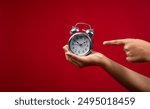 Holding an alarm clock in hand and pointing finger at it, Time and offer concept image, Woman hand holding alarm clock isolated on red background with copy space