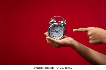 Holding an alarm clock in hand and pointing finger at it, Time and offer concept image, Woman hand holding alarm clock isolated on red background with copy space - Powered by Shutterstock