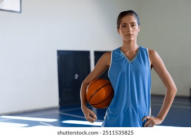 Holding basketball, female basketball player standing confidently on indoor court, copy space. Sports, athlete, confidence, indoors, competition, fitness - Powered by Shutterstock