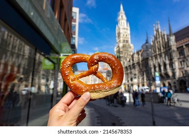 holding bayern style pretzel on the victuals market with Neues Muncher Rathaus background in munich - Shutterstock ID 2145678353