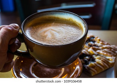 Holding A Big Brown Coffee Mug With Coffee Moments With Latte Art And A Wonderful Delicious Hot Coffee And Cozy Start To The Morning With Bagel And Breakfast Ready To Go