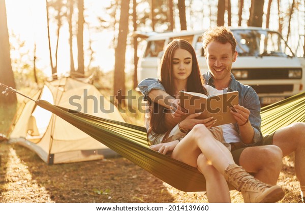 Holding book. Young couple is traveling in the\
forest at daytime\
together.