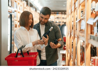 Holding the bottle. Man and woman are choosing wine in the shop. - Powered by Shutterstock