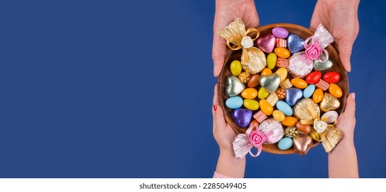 Holding bowl of candies,  top view image of woman and child hand holding bowl of candies. Isolated dark blue background, copy space. Ramadan feast celebration concept idea. Greetings banner.