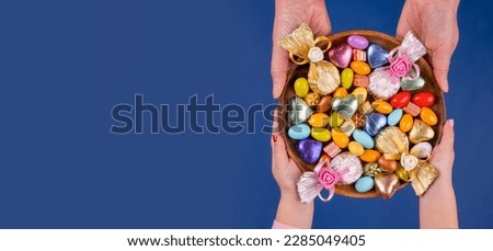 Holding bowl of candies,  top view image of woman and child hand holding bowl of candies. Isolated dark blue background, copy space. Ramadan feast celebration concept idea. Greetings banner.
