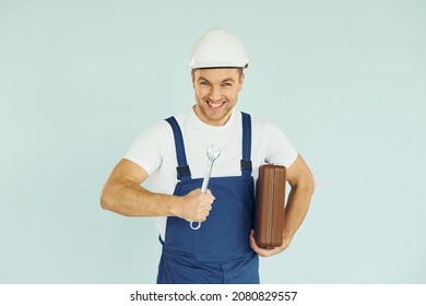 Holding Brown Case. Worker In Uniform And Hard Hat Standing In The Studio With Equipment.