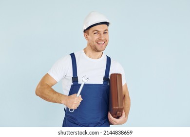 Holding Brown Case. Worker In Uniform And Hard Hat Standing In The Studio With Equipment.