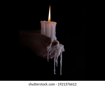 Holding a candle in the dark with melted wax dripping over the hands