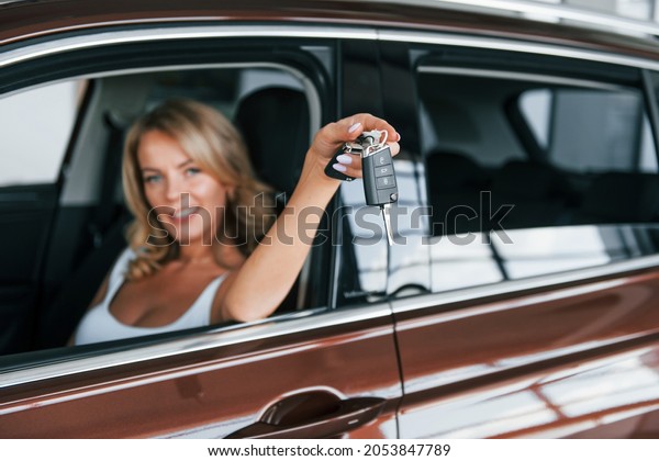Holding car keys. Woman in formal clothes is\
indoors in the\
autosalon.