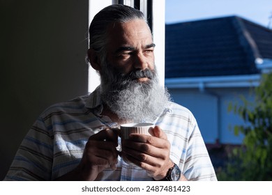 Holding cup, senior man with beard enjoying morning sunlight indoors. Elderly, lifestyle, beverage, relaxation, mindfulness, contentment - Powered by Shutterstock