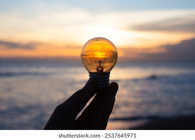 holding an electric light bulb in his hands on the sea coast at sunset - Powered by Shutterstock