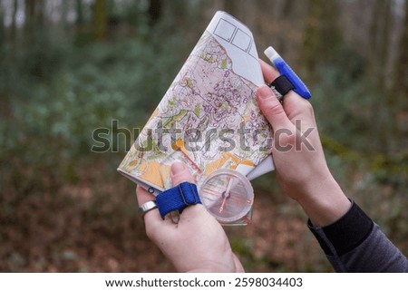 Holding forest orienteering map with both hands. Compass on the left hand, SI-card on the right hand with forest background