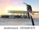 Holding a fuel nozzle against with gas station blurred background