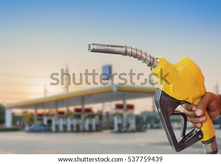 Holding a fuel nozzle against with gas station blurred background.
