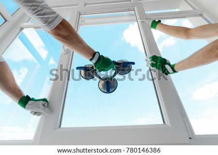 Holding glass with a vacuum lifter. Two guys installing a window in a new building. Construction site, industrial job.