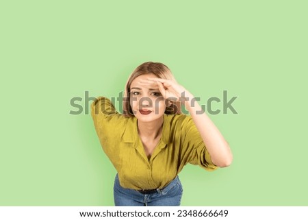 Holding hand at forehead,  young blonde girl leaning forward smiling looking camera paying attention holding hand at forehead. Isolated over light green background, copy space. Lifestyle concept.