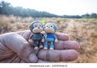 holding in the hand of two plastic monkey toys found at the grassy field