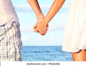 Holding hands couple on beach. Romantic love and happiness concept image with happy young couple. Closeup.