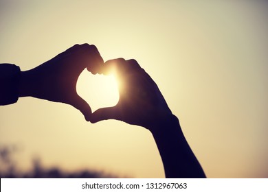 holding hands in heart shape at sunrise beach - Shutterstock ID 1312967063
