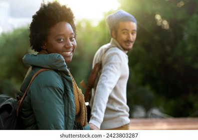 Holding hands, park and happy interracial couple together with smile, bag and morning commute to university. College, students and romance in nature, man and woman with diversity, mockup and love. - Powered by Shutterstock