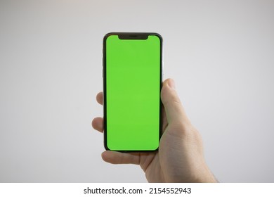 Holding an iPhone in hand. Green Screen on the phone. Mock-up of an iPhone. Apple product in hand. Vertical tilt of the phone.