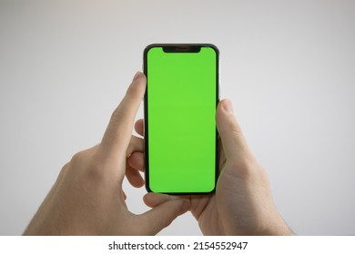Holding an iPhone in hand. Green Screen on the phone. Mock-up of an iPhone. Apple product in hand. Vertical tilt of the phone.