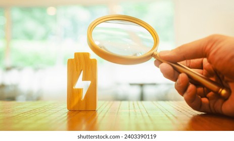 ฺBusinessman holding a magnifying glass to electric symbol .Technology battery high power electric energy with a connected charging cable. Battery to electric cars and mobile devices. - Powered by Shutterstock