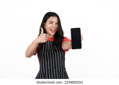 Holding mobile smartphone, Food shop owner concept, Smiling young confident asian woman in black apron and red t-shirt isolated on white background.