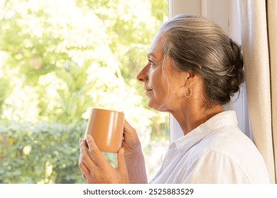 Holding mug, mature woman looking out window, enjoying peaceful moment, copy space. Contemplation, relaxation, tranquility, serene, coffee, happiness - Powered by Shutterstock