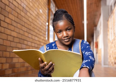 Holding notebook, african american girl smiling and reading in school hallway, wearing backpack. Education, student - Powered by Shutterstock