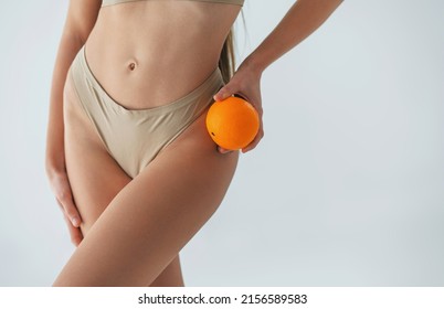 Holding orange fruit. Woman in underwear with slim body type is posing in the studio.