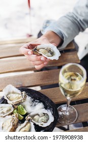 Holding an oyster, a plate of oysters, a glass of sparkling wine on a wooden table 