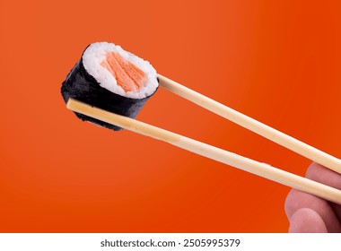 Holding piece of urumaki sushi roll with chopsticks isolated orange background - Powered by Shutterstock