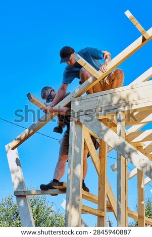 Holding rafter leg together while tightening screw, workers assemble roof truss.