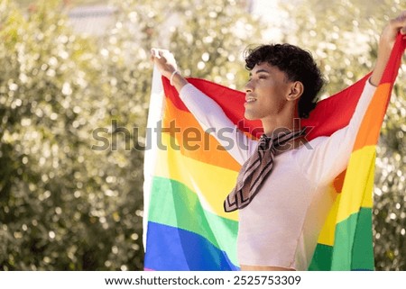 Holding rainbow flag, young man celebrating LGBTQ+ pride outside with joyful expression. celebration, equality, diversity, inclusivity, community, love