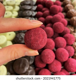 Holding A Raspberry Truffle Over An Open Display Case Full Of Handmade Candies 